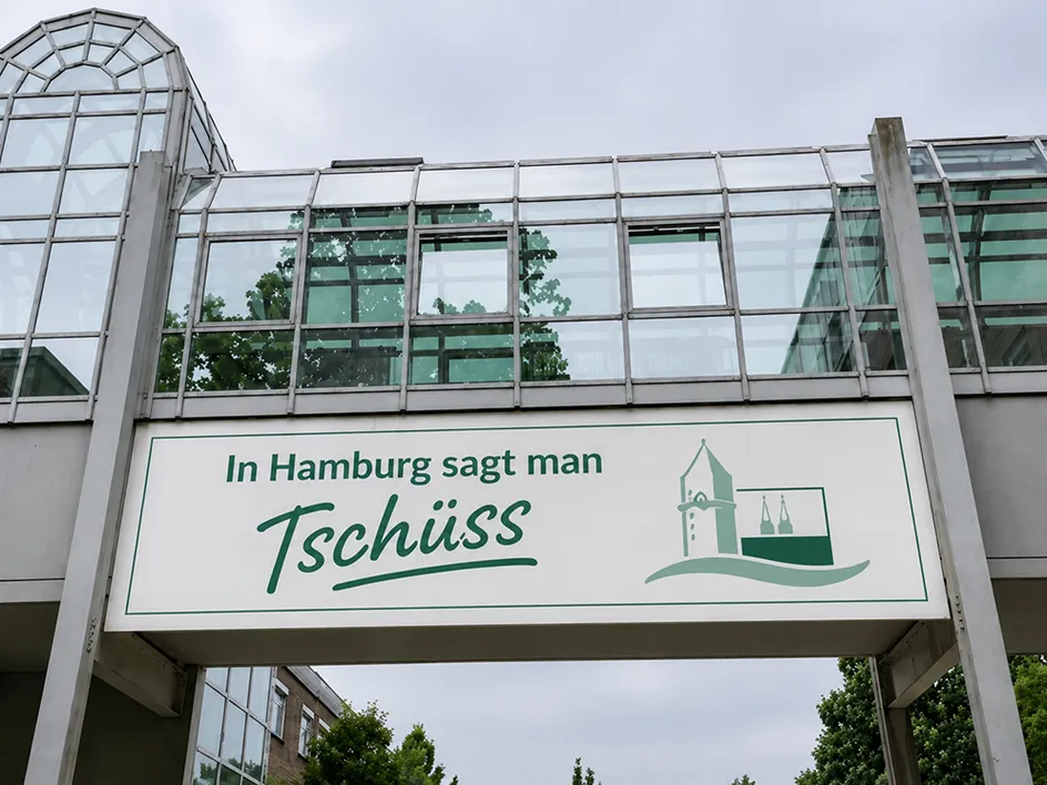 Schilder mit dem Spruch ‚In Hamburg sagt man Tschüss‘ vor einem modernen Gebäude.