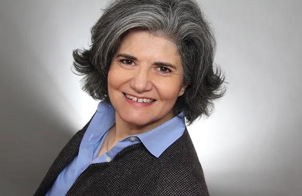 Portrait of a smiling woman with graying hair wearing a blue shirt and a dark blazer.