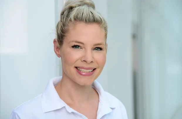 Portrait of a smiling woman with blonde, updo hairstyle against a light background.