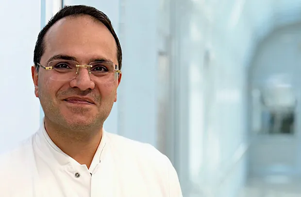 Portrait of a smiling man wearing glasses in a white shirt against a bright background.