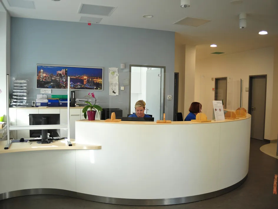 Reception desk with two people behind a semi-circular counter, brochures nearby and a city view on the wall.